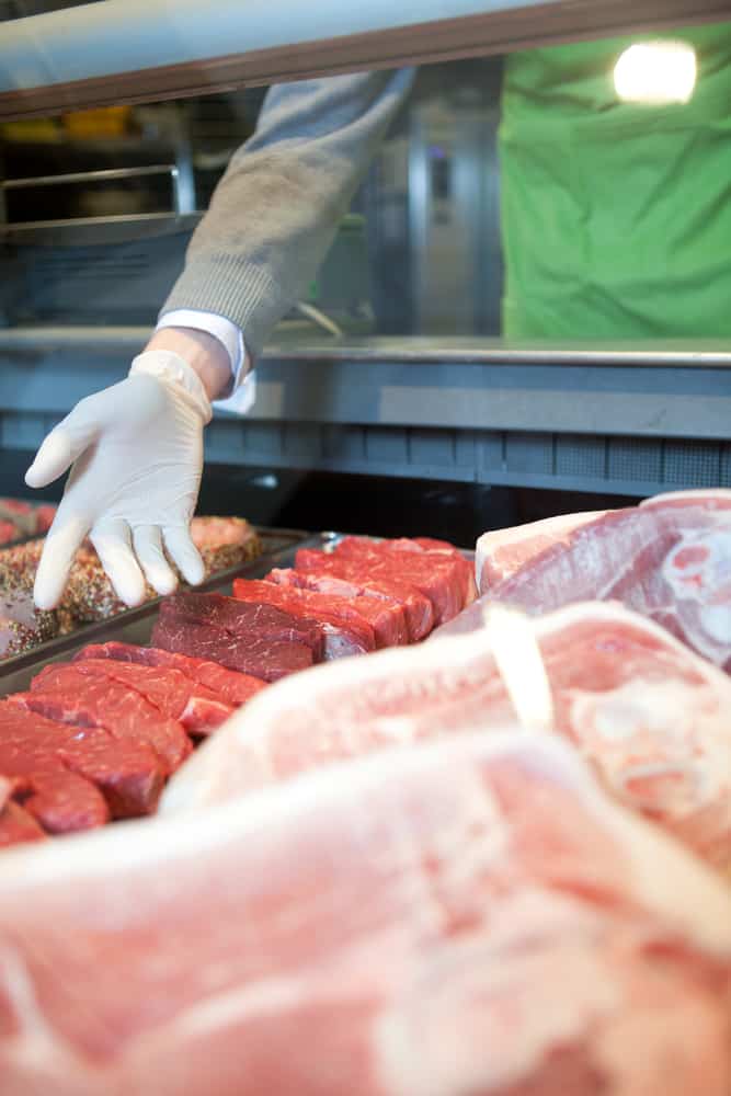 A hand showing the various meat options at a fresh meat counter